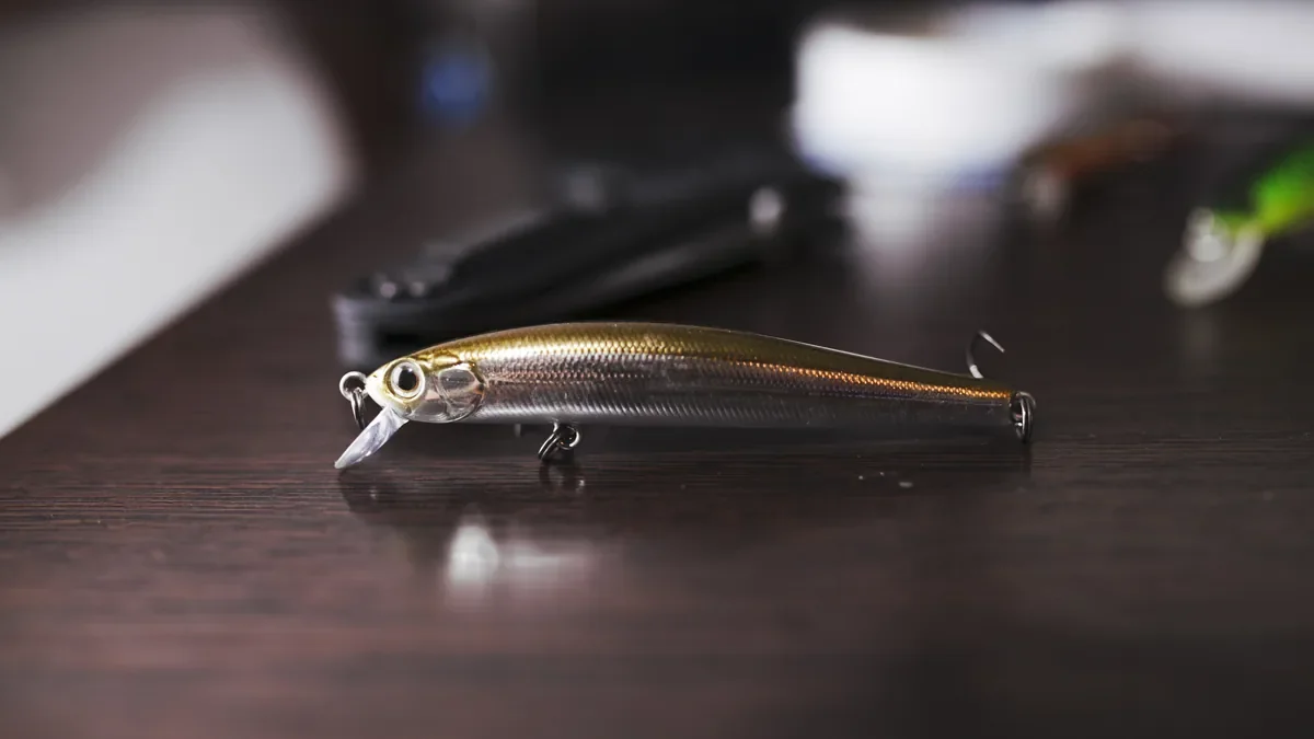 A gold fishing lure with hooks resting on a dark wooden desk