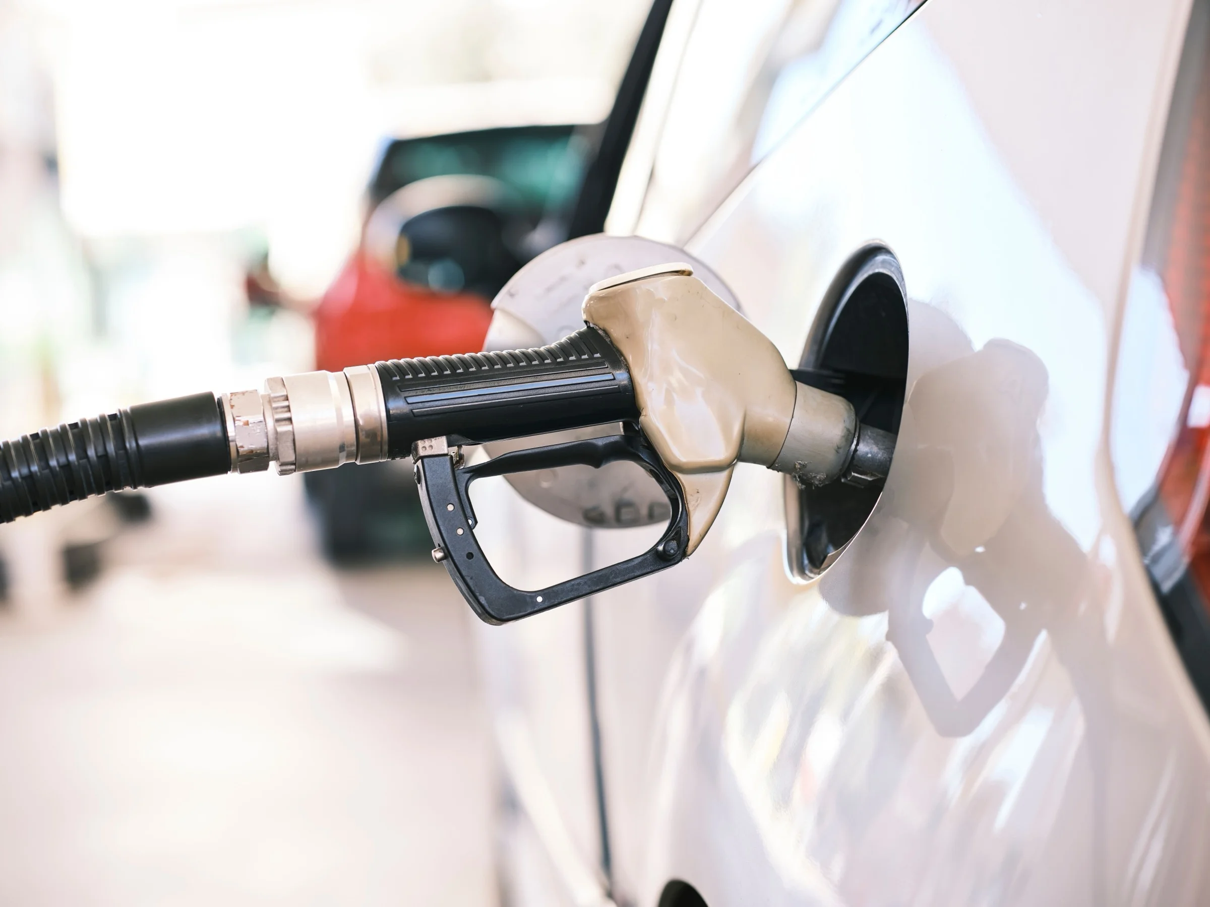 Fuel nozzle filling a white car at a petrol station