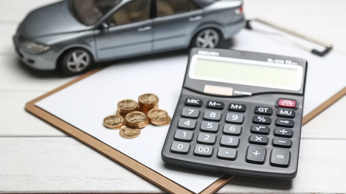 Model car beside a calculator and a small stack of coins on a clipboard