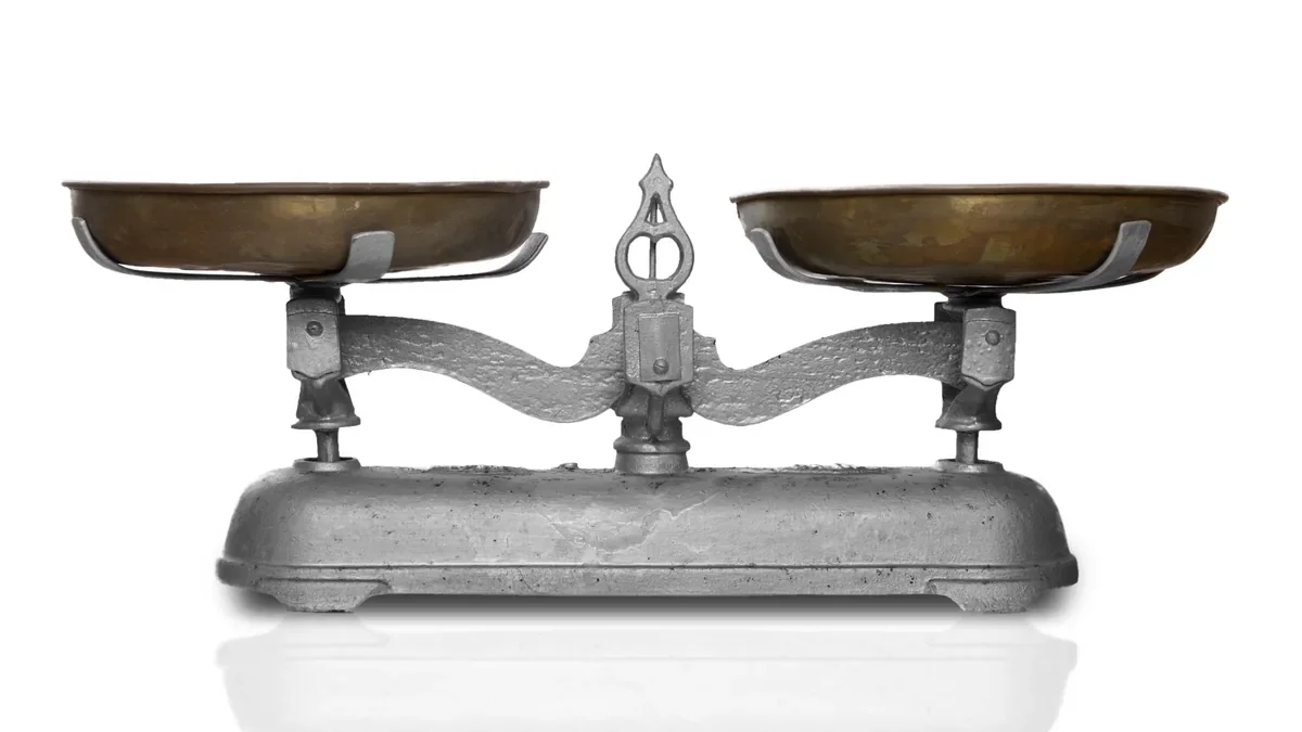 An old metal balance scale with two empty brass pans on a white surface