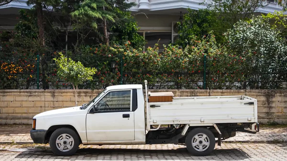 White single-cab work ute with a drop-side tray parked on a paved street