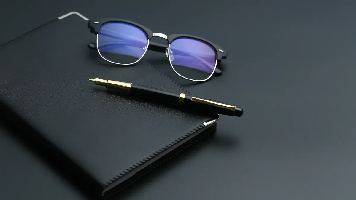 Closed black notebook with a fountain pen and glasses on a dark desk