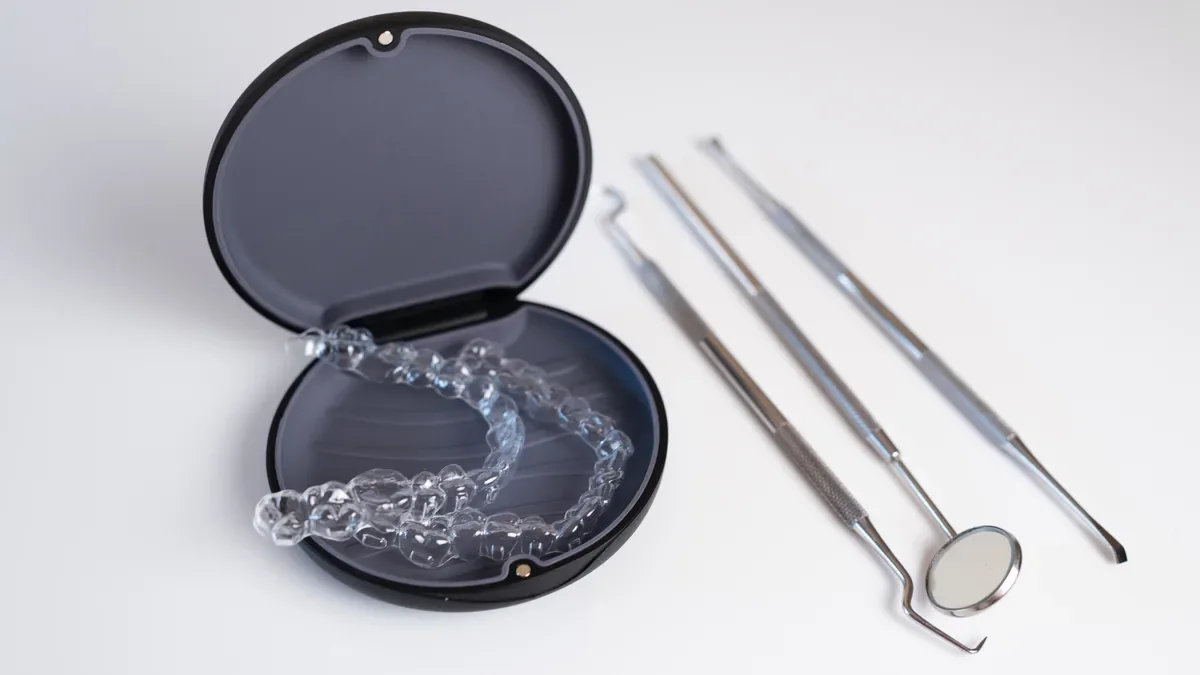 Clear aligners in an open black case beside dental tools on a white surface