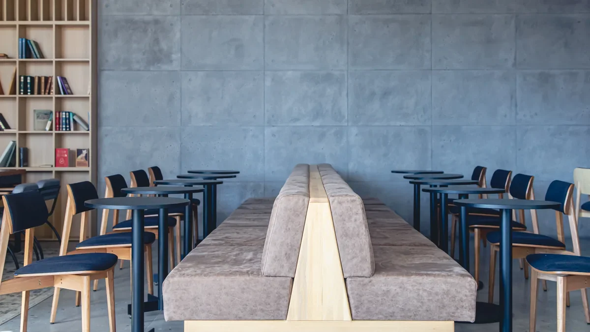Empty cafe interior with bench seating, small tables and chairs against a concrete wall
