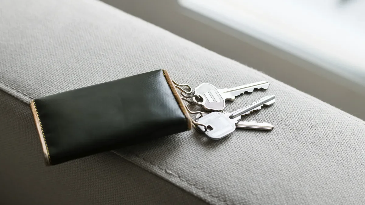 A set of house keys sliding out of a dark leather key pouch on the arm of a grey fabric sofa