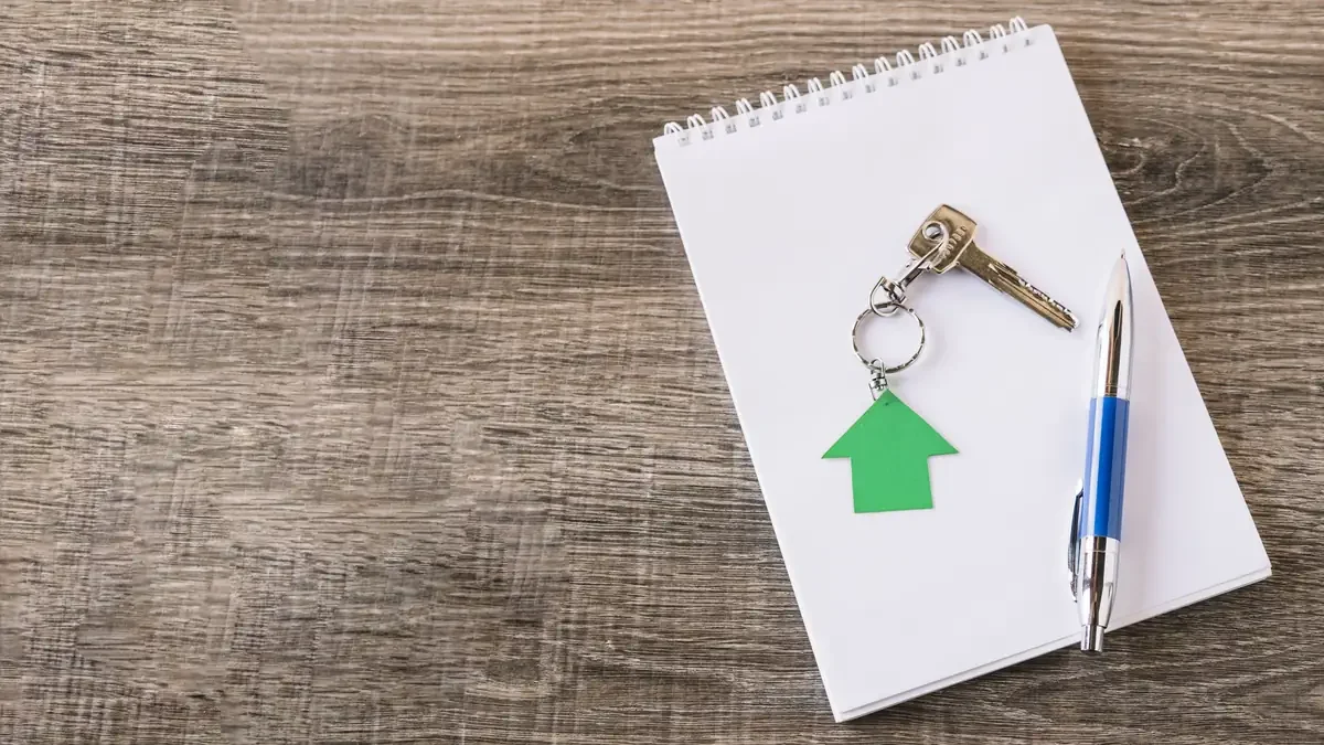 Keys with a green house-shaped tag and a pen resting on a blank notepad
