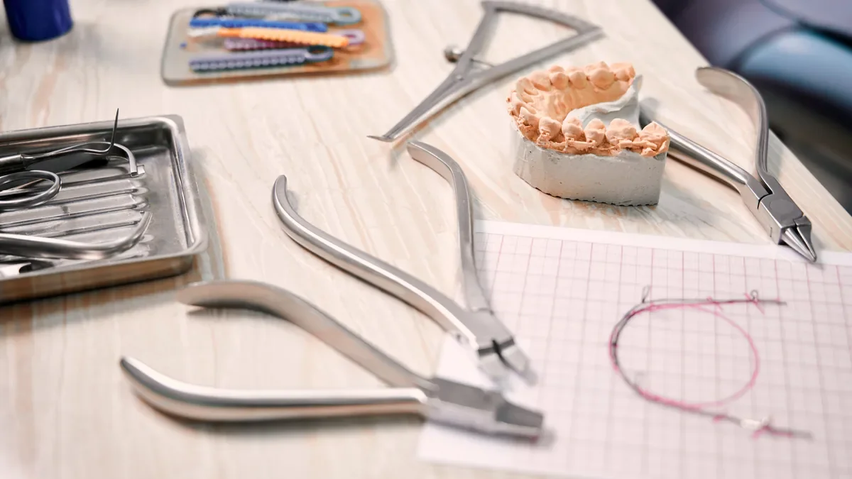 Orthodontic pliers, a plaster teeth model and a coiled wire on a desk beside a tray of instruments