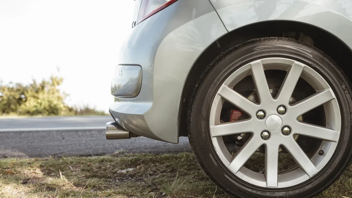 Rear wheel and alloy rim of a silver hatchback parked beside a road